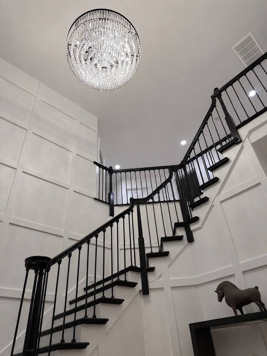 Renovated staircase with black railings, paneled walls, and a crystal chandelier